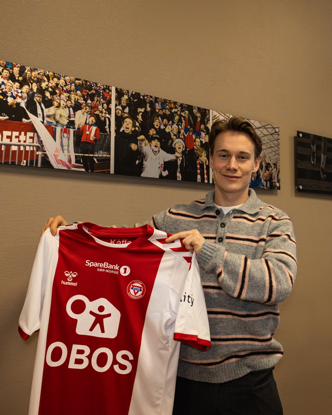 <em>Rasmus foran Profetene-bilder i klubbstua. Nå satser han på å glede KFUM-kamerater med mål og målpoeng. Foto: Markus Bratlie</em>